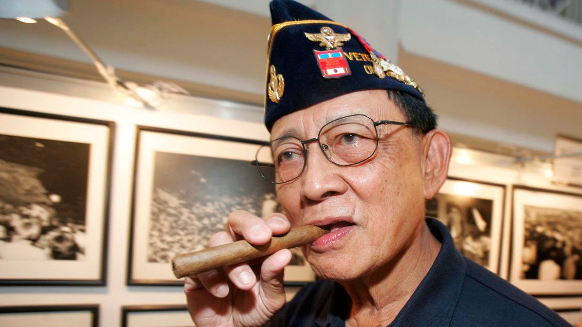 Former Philippine President Fidel Ramos bites his cigar as he looks on photographs during an...