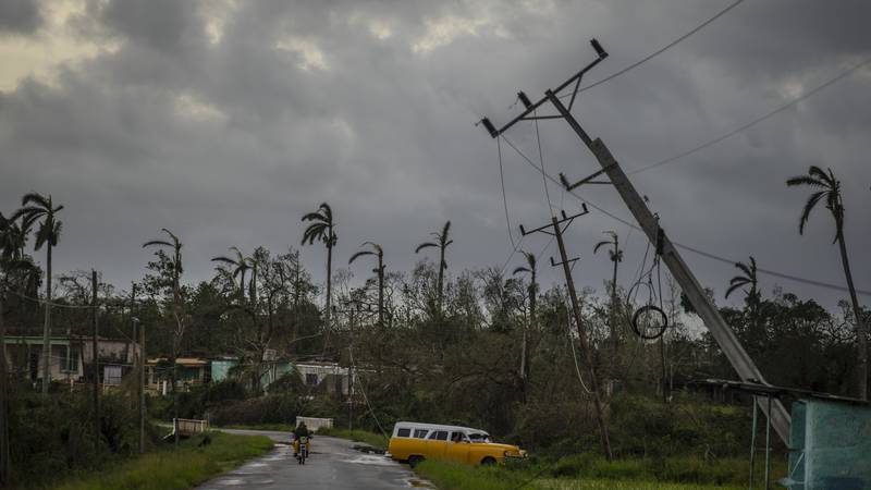 A classic American car drives past utility poles tilted by Hurricane Ian in Pinar del Rio,...