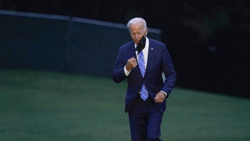 President Joe Biden takes off his mask as he walks off of Marine One on the South Lawn of the...