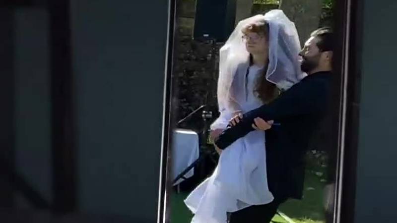 A wedding video showing the groom walking down the aisle holding his sister-in-law is going...