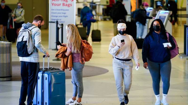 FILE - Travelers wearing protective masks as a precaution against the spread of the coronavirus...