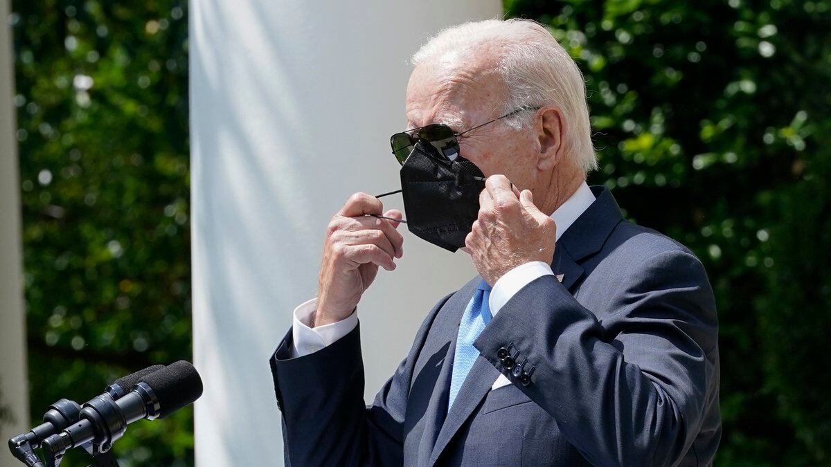 President Joe Biden removes his face mask as he arrives to speak in the Rose Garden of the...